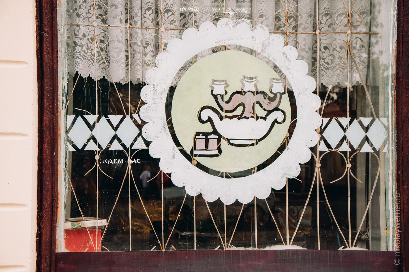 Окно магазина. Решётка, тюль за стеклом. Нарисован подсвечник в круге с орнаментом.